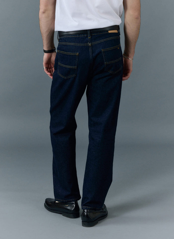 A model seen from behind wearing the Percival Straight Leg Denim Jeans in dark indigo with a white t-shirt and black loafers.