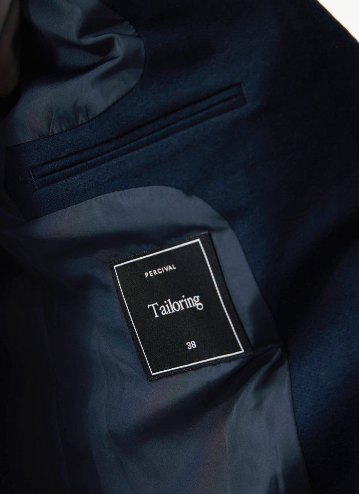 A close-up of the interior of the navy Moleskin Blazer, showing the Percival Tailoring label, lining, and internal pocket.