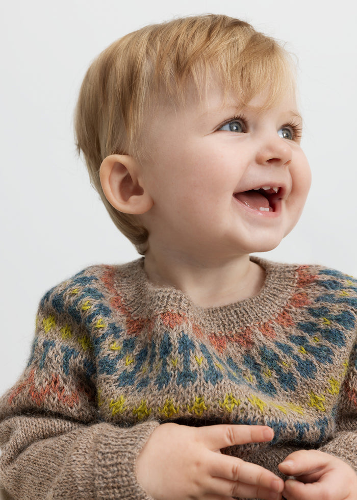 Baby smiling wearing beige wool knit blouse with colored yoke