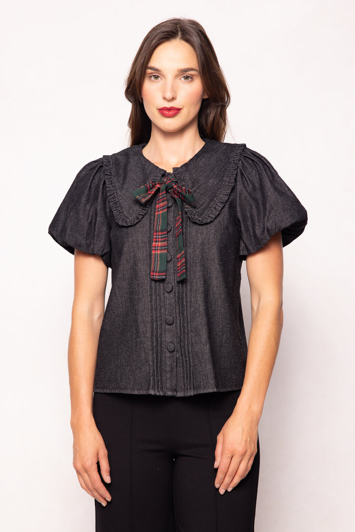 Woman wearing a dark denim blouse with a plaid collar against a white background