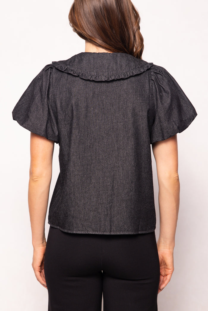 Person wearing a dark denim blouse with ruffled shoulders on a white background