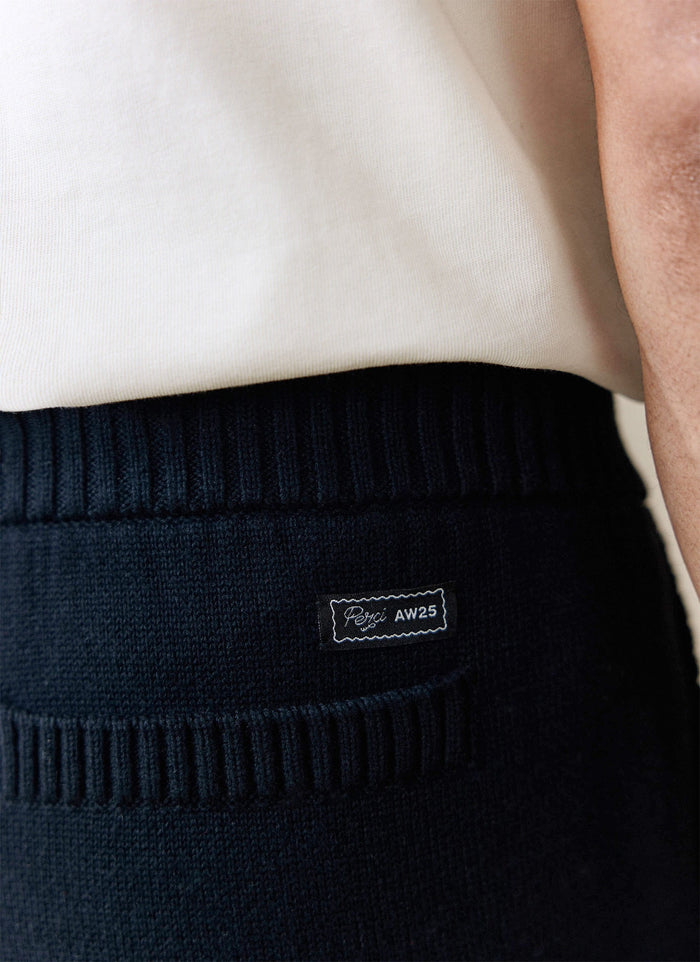 A close-up of the black knitted Chronicle Trackpant from Percival, showing the woven brand label on the back pocket.