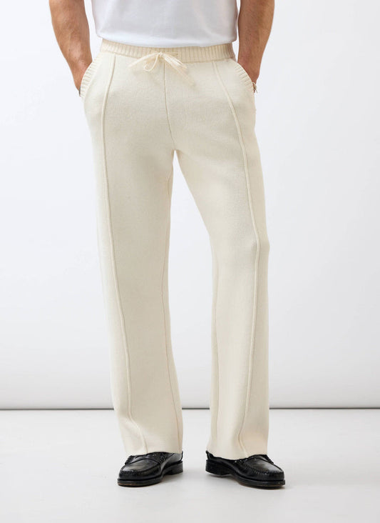 A model wears the Percival Chronicle Knitted Straight Leg Trackpant in ecru cotton, paired with smart black loafers.