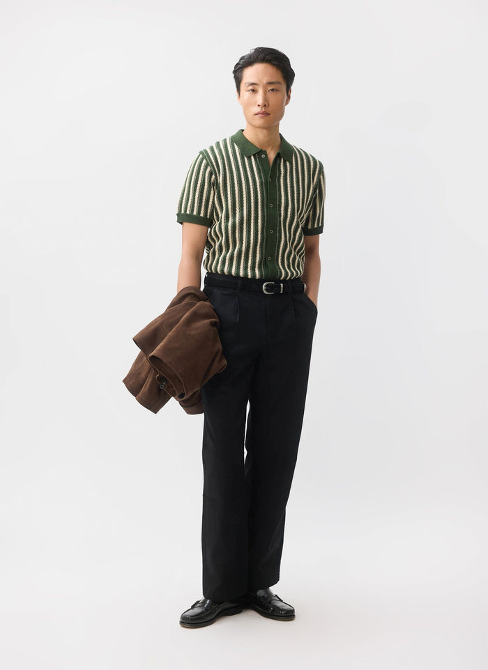 A model wears the Percival Collins Knitted Shirt in green with vertical stripes, paired with black trousers and loafers.
