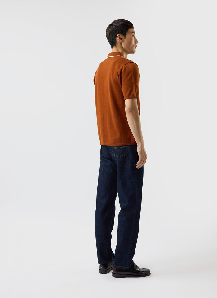 A model wears the Percival Contrast Trim Shirt in rust, a knitted wool polo, styled with dark jeans and loafers.