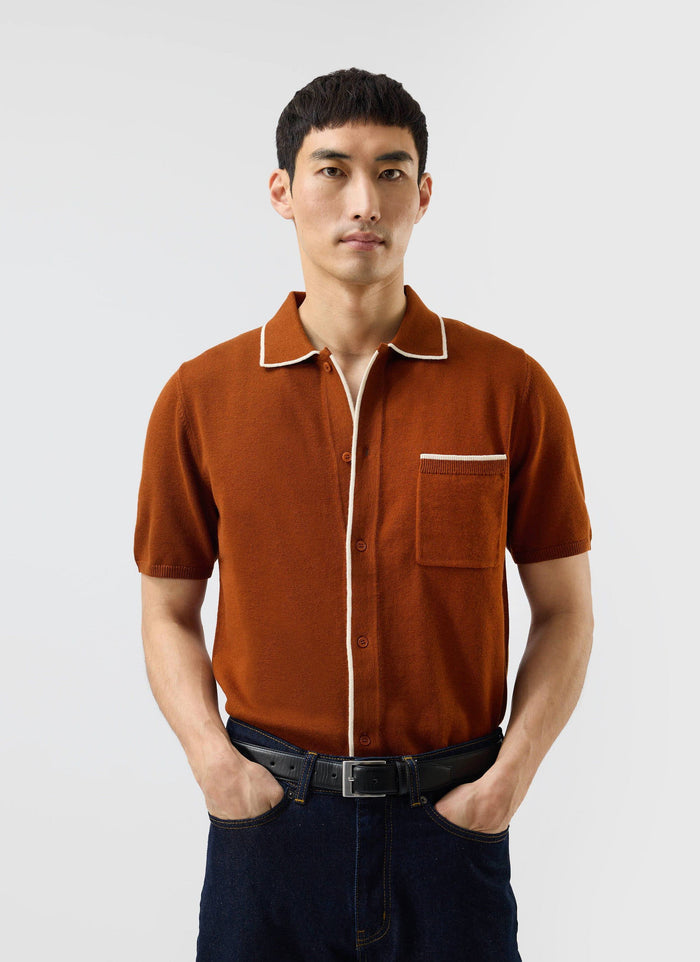A man models the rust Percival Contrast Trim Shirt, a knitted wool-blend polo with white piping, paired with dark jeans.
