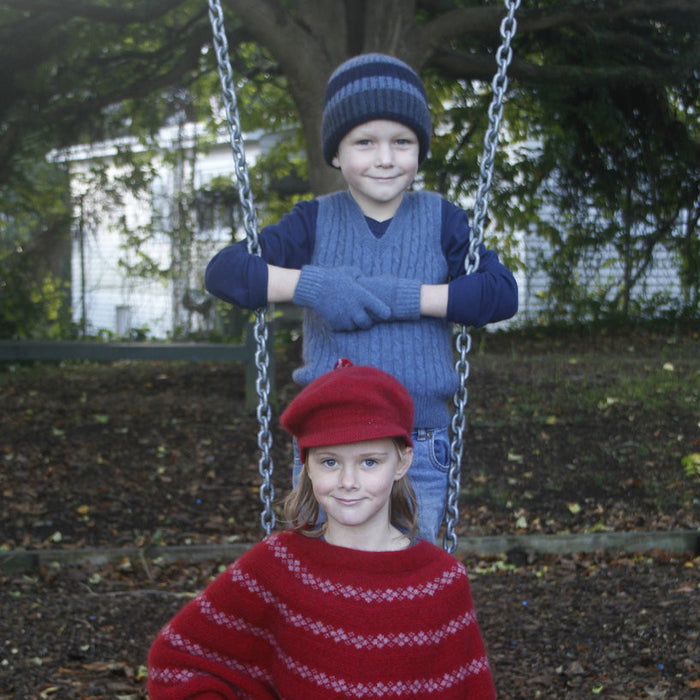 Boy wearing light blue colour vest, standing behind girl on a swing.