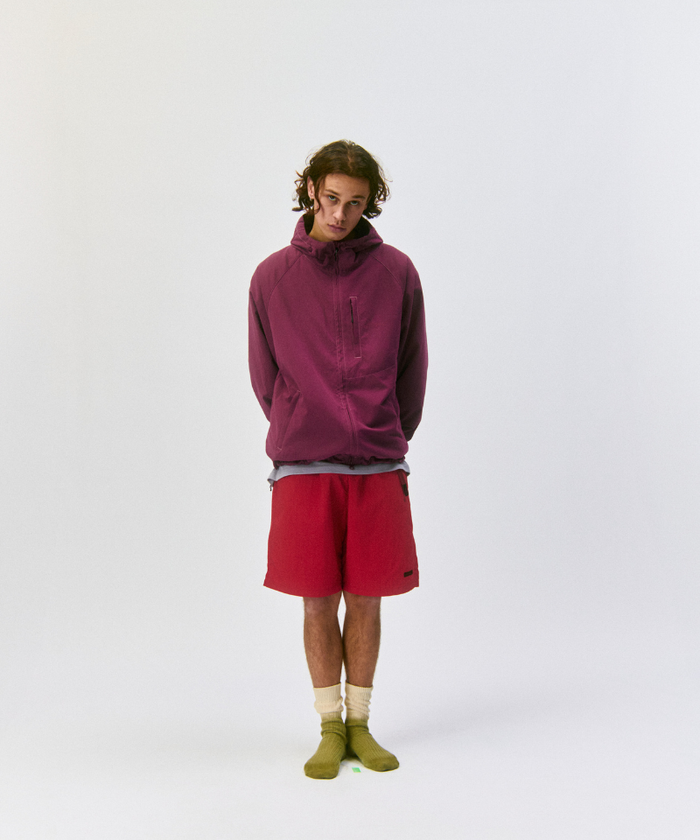 Person wearing a maroon pullover, red shorts, and Cactus colored Gramicci Dip Dye Socks against a light-tone background.