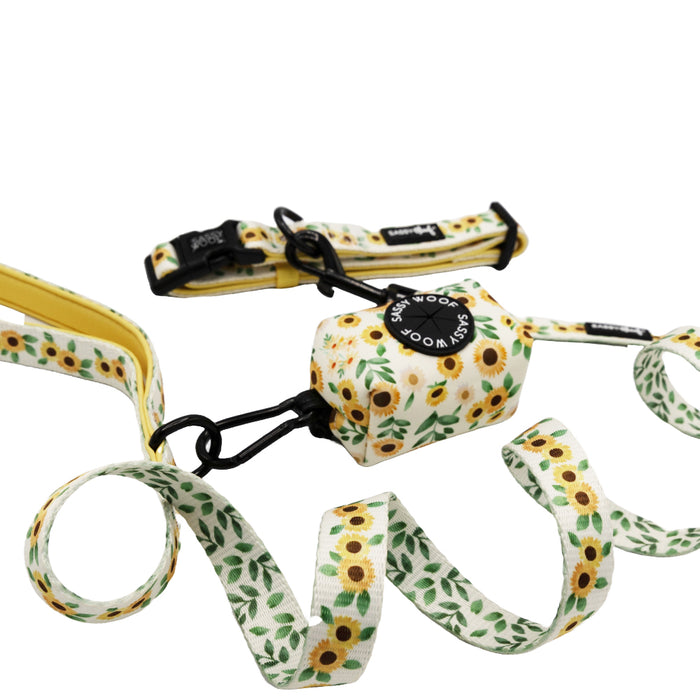 Introducing the Sassy Woof Dog Collar Three Piece Bundle – Sunflower Dreams: a sunflower-patterned leash, paired with a matching waste bag holder and coordinating collar. Each piece features vibrant yellow sunflowers and green leaves on a crisp white background for a perfectly coordinated look.