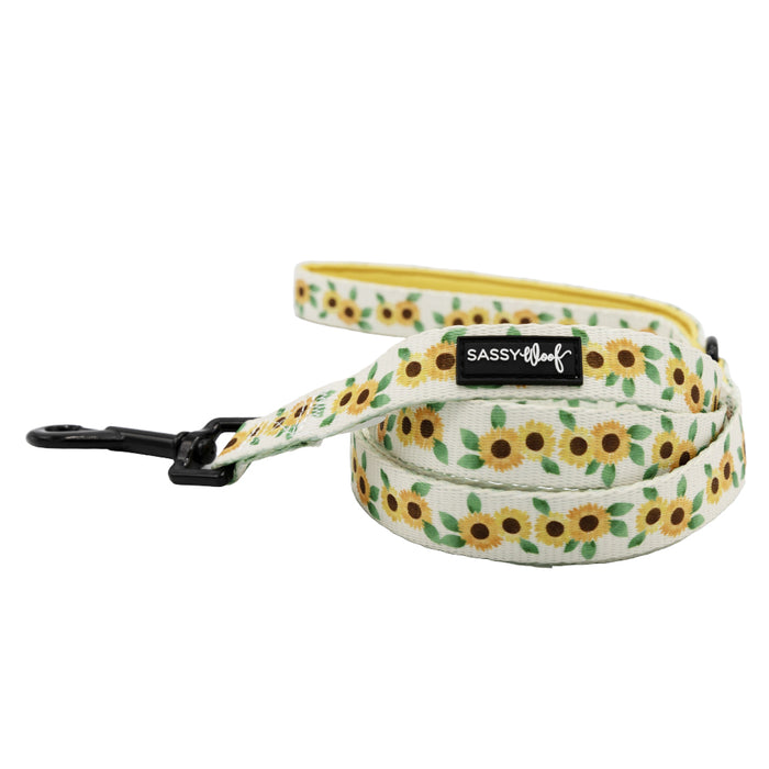 Introducing the Sassy Woof Dog Collar Three Piece Bundle - Sunflower Dreams: This rolled-up leash boasts a cheerful sunflower pattern, a sturdy black metal clasp, and the signature SASSY WOOF label. Designed to perfectly pair with the matching sunflower dog collar and coordinating waste bag holder, it’s an effortless way to bring style and function to every walk.