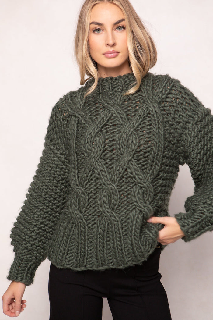 A woman models the Ivy City Co Erica Sweater in Emerald, styled with black pants and posing with one hand on her hip against a light background.