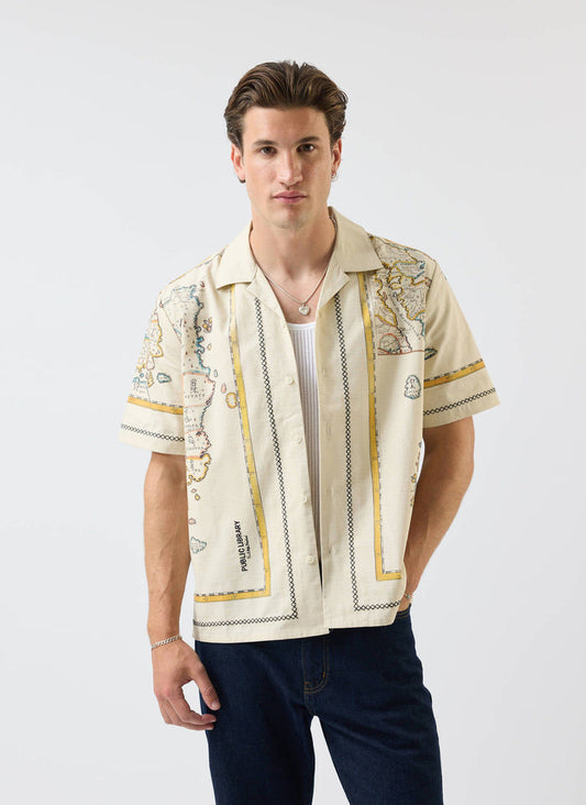 A man models the Percival Ex Libris Cuban Shirt in ecru, featuring a map-inspired print and worn over a white vest.