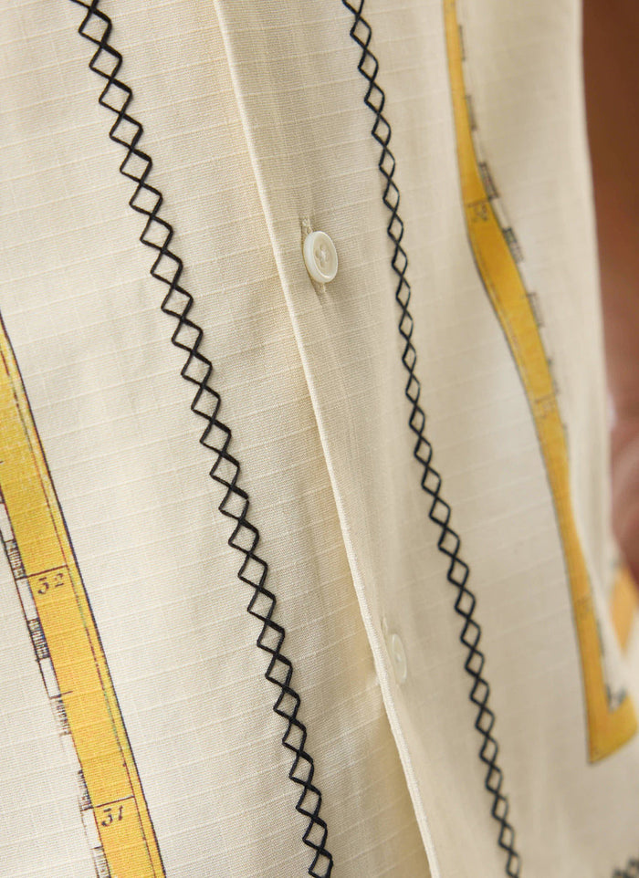 A close-up of the Percival Ex Libris Cuban Shirt, showing the ecru cotton ripstop, black cross-stitch embroidery and artwork.