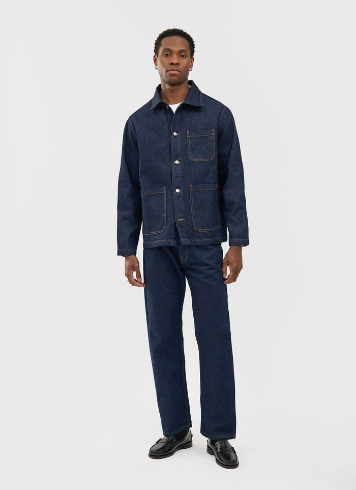 A model wears the Percival Gove Chore Jacket and matching jeans in dark indigo denim against a plain studio background.