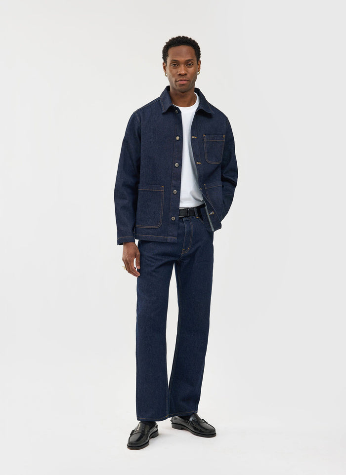 A model wears the Percival Gove Chore Jacket in dark indigo, styled as a co-ord with matching jeans and a white t-shirt.