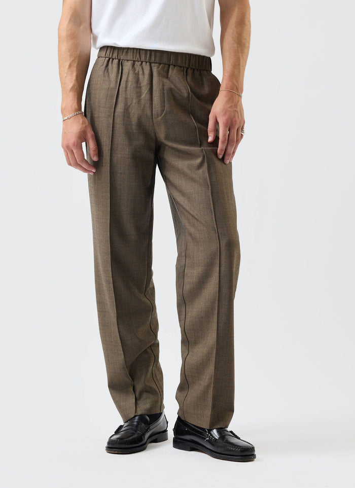 A model wears the Percival Grounds Relaxed Trousers in Oak herringbone wool, styled with a white t-shirt and black loafers.