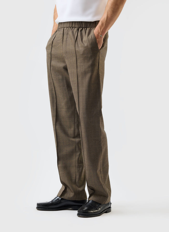 A model wears the Percival Grounds Relaxed Trousers in oak herringbone wool, shown in a side profile with black loafers.