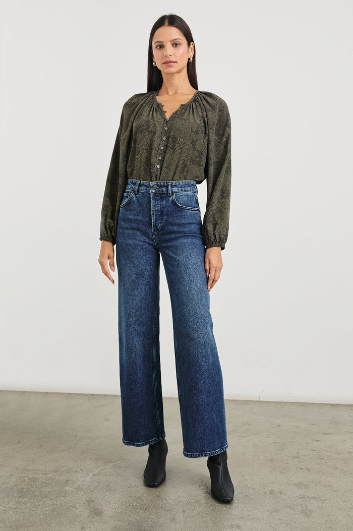 Indi Top with a V Neckline with a Button Placket, Pleating at Back Neckline and Elastic Cuffs in Olive Pebble Colorway, with black pebbles on olive - Front tucked Full Body View Featured on Model