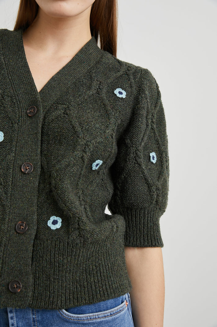 Isla Mid-length-Sleeve Cardigan with Ribbed Hems and Cuffs and Button Closure in Forest Daisies Colorway, with blue crochet daisies on forest green - Front View Featured on Model