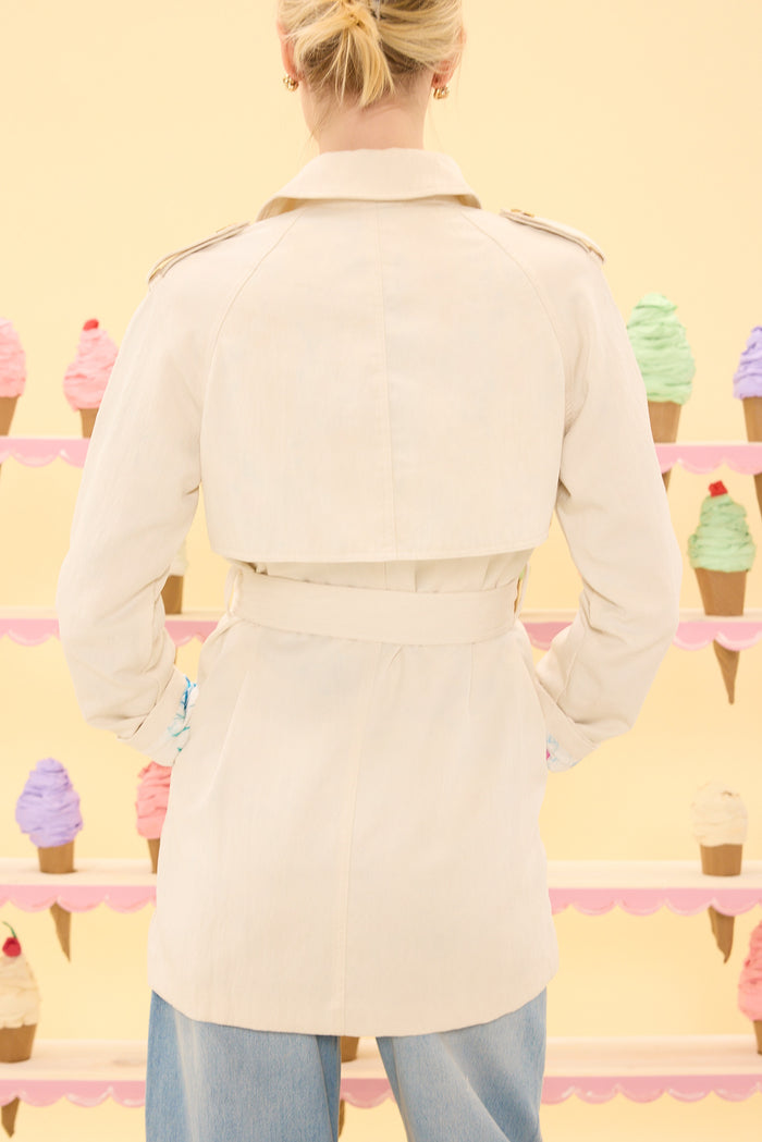 Person wearing a beige trench coat standing in front of ice cream cones on a yellow background