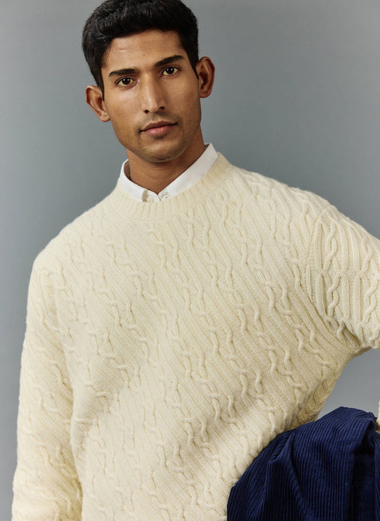 A model wears the Percival Melville Cable Knit Jumper in ecru, layered over a white shirt against a grey studio background.