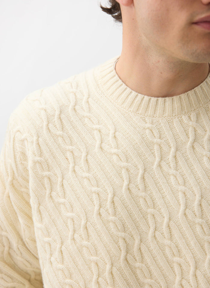 Close up of a model wearing the Percival Melville Cable Knit Jumper in ecru, showcasing the intricate diagonal knit detail.