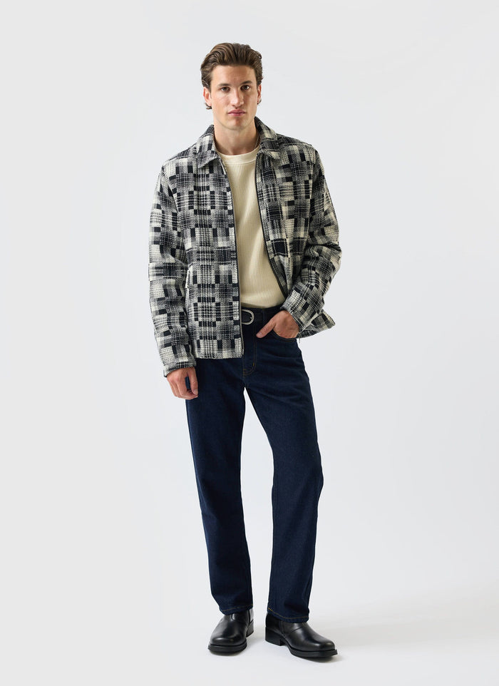 A model wears the Percival Glossary Patchwork Jacket in grey, styled with a cream jumper and dark jeans.