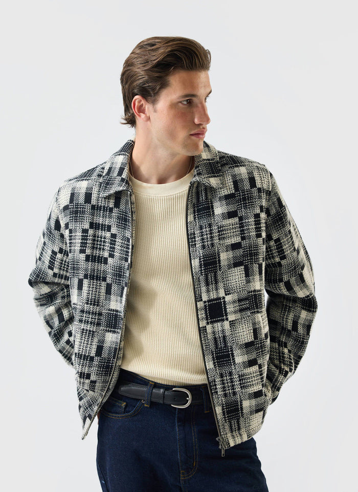 A model wears the Percival Glossary Patchwork Jacket in grey twill, styled over a cream knit top and dark denim jeans.