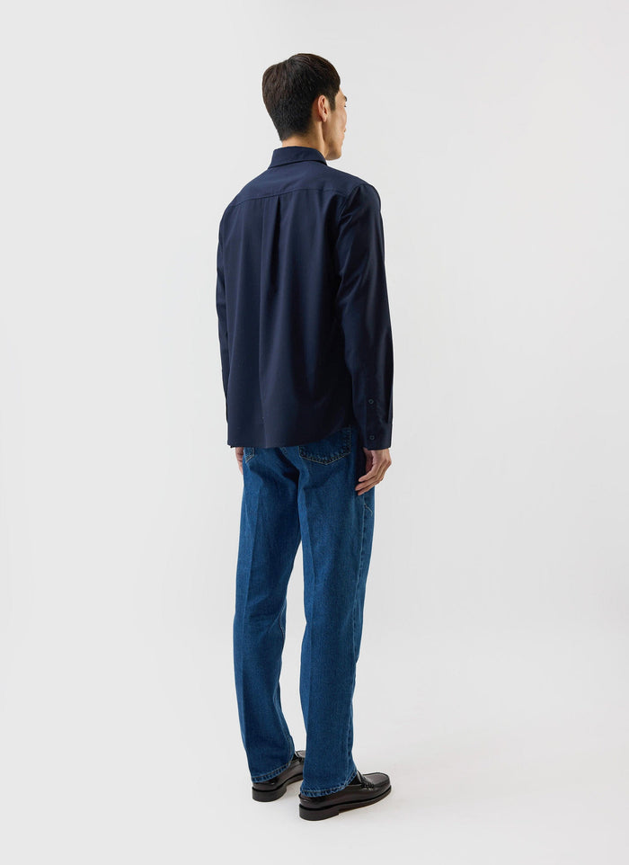 A man models the back of the navy blue Percival x Warren Pleated Shirt, showing its relaxed, oversized fit.