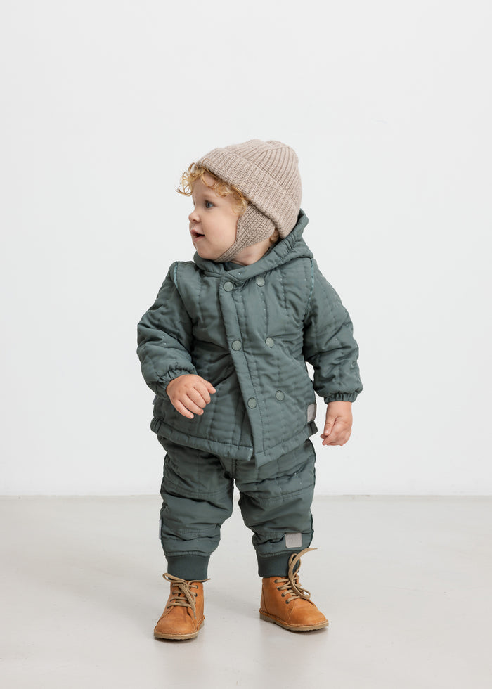 Baby wearing dusty green thermal jacket and pants, standing and looking to the side