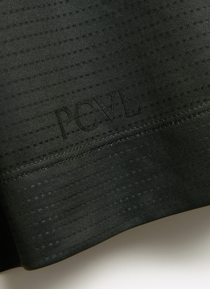 A close-up of the tonal PCVL logo embossed on the hem of the forest green Performance Top by Percival.