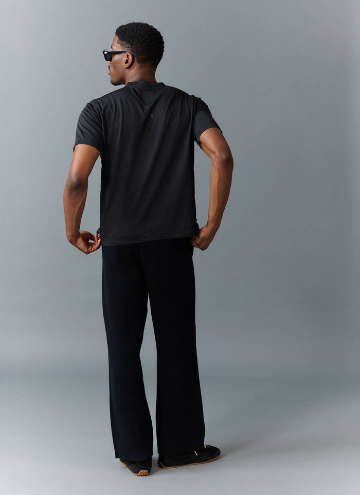 A model wears the black PCVL Printed Performance T-shirt from Percival, showing the back detail.