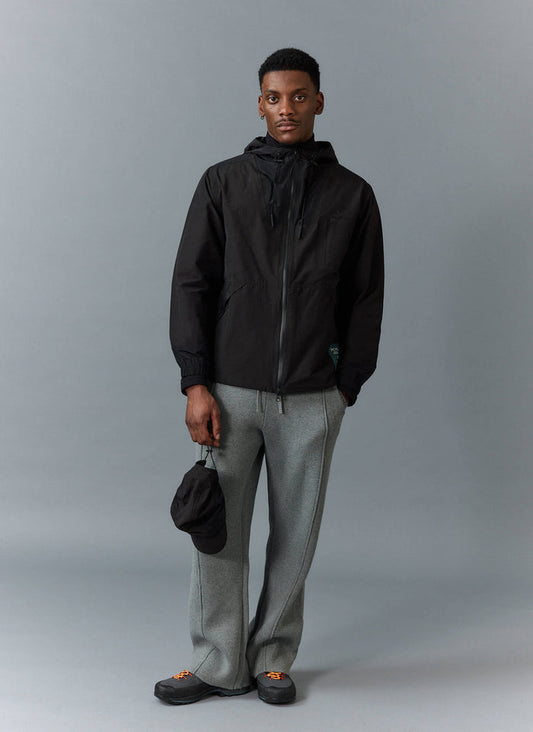 A model wears the black PCVL Zip Through Water Resistant Jacket from Percival, styled with grey trousers.