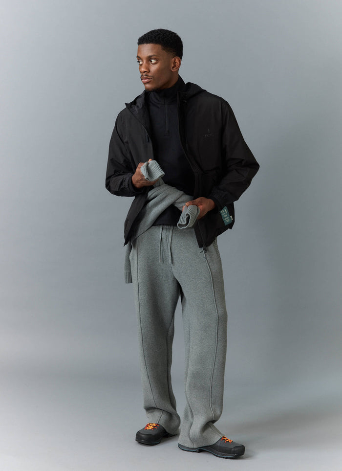 A model styles the black Percival PCVL Zip Through Water Resistant Jacket with a black base layer and wide-leg grey trousers.