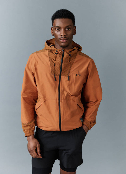 A model wears the Percival PCVL Zip Through Water Resistant Jacket in rust, styled with black shorts against a grey backdrop.