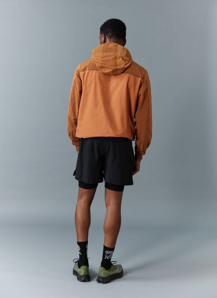 A model seen from behind wearing the Percival PCVL Zip Through Water Resistant Jacket in rust with black shorts.