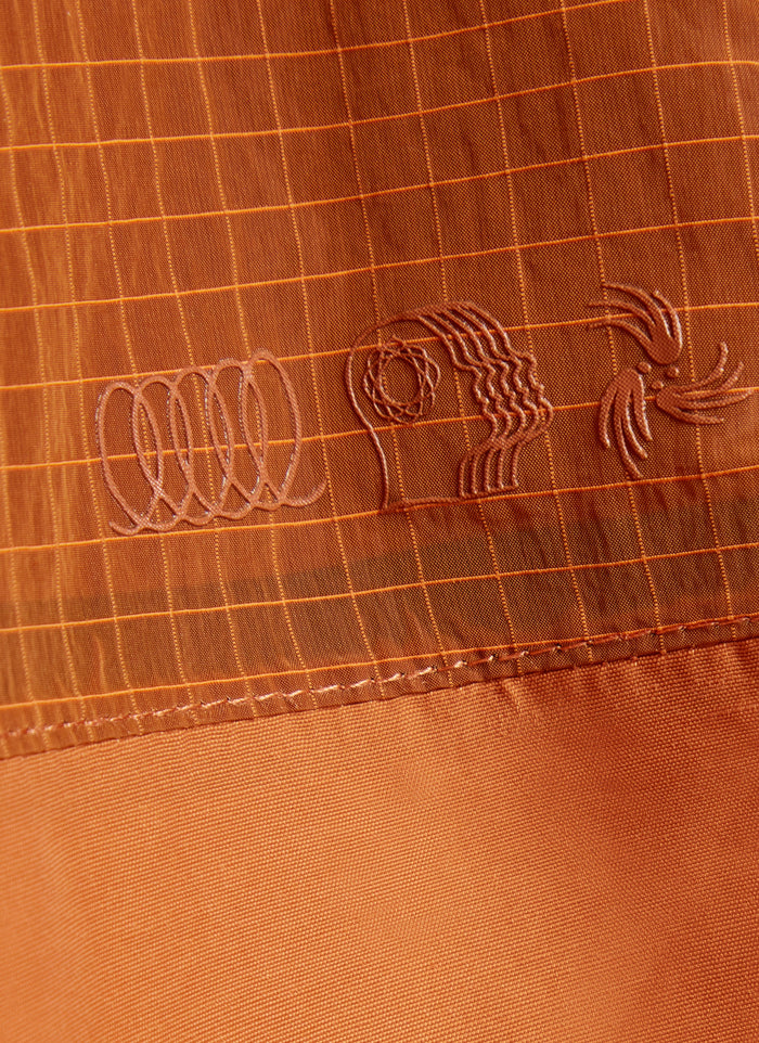 Close-up of the tonal PCVL logo on the rust water-resistant jacket from Percival, showing the technical grid fabric.
