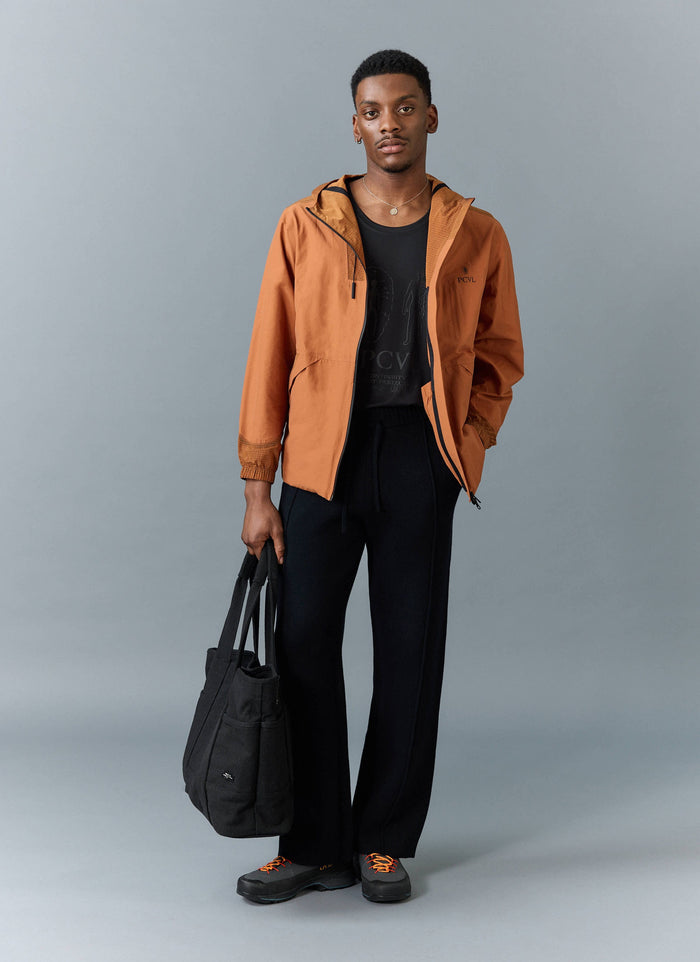 A model wears the Percival PCVL Zip Through Water Resistant Jacket in rust, styled with a black tee and trousers.