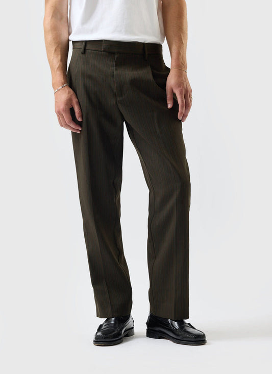 A model wears the Percival Pleated Tailored Chapter Trousers in forest green, styled with a white t-shirt and black loafers.