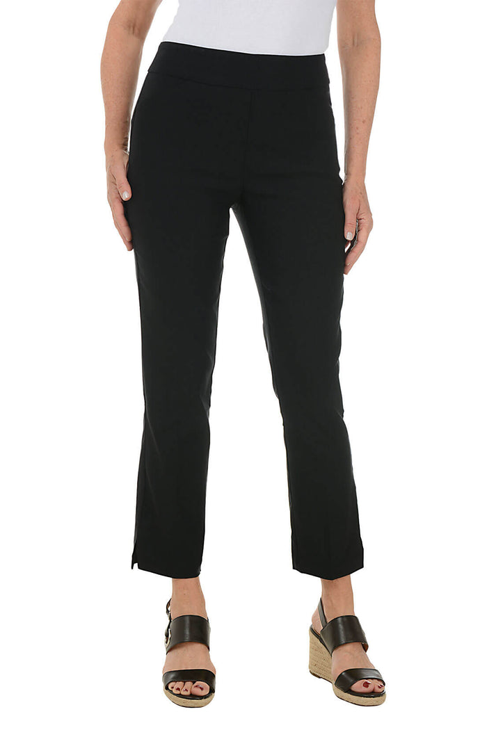A front shot of a model wearing a pair of black ankle pants with an elastic waistband, dual front pockets, and side slits on the hemline. The pants are pull-on style with no visible zipper.