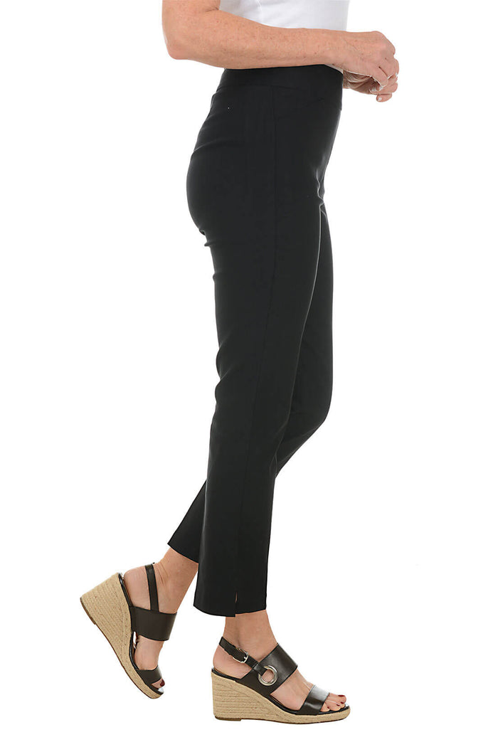 A side shot of a model wearing a pair of black ankle pants with an elastic waistband, dual front pockets, and side slits on the hemline. The pants are pull-on style with no visible zipper.