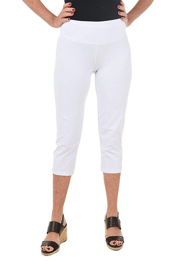 A front shot of a model wearing a pair of white pull-on slimming capri pants with a mesh tummy control panel.