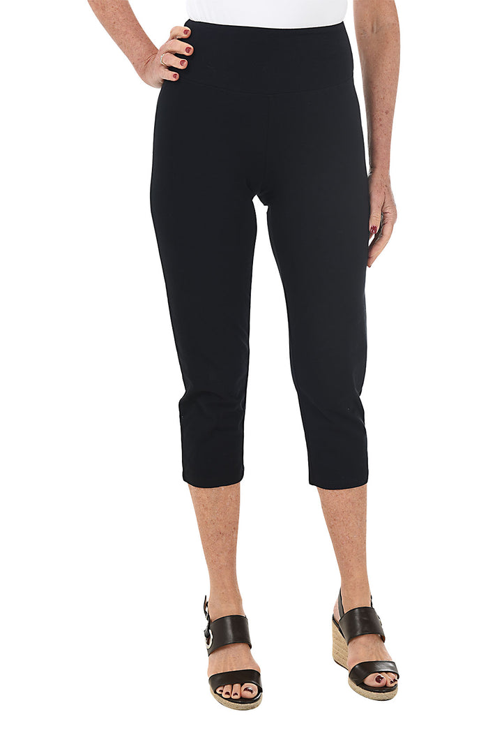 A front shot of a model wearing a pair of black pull-on slimming capri pants with a mesh tummy control panel.