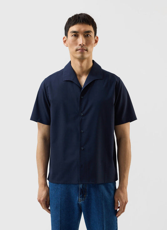 A model wears the navy blue Relaxed Cuban Drape Shirt from the Percival x Warren collaboration against a white background.