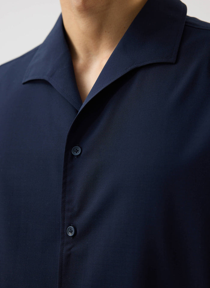 A close-up of a model wearing the Percival x Warren Cuban Drape Shirt in navy blue, showing the collar and button detail.