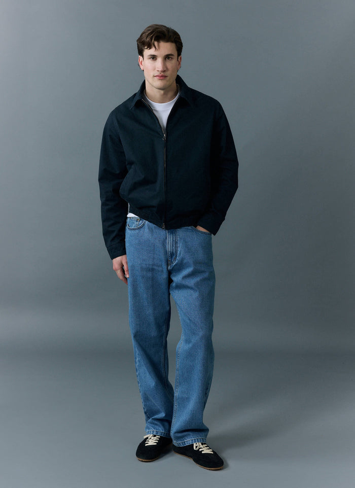 A man models the Percival Wide Leg Denim Jeans in light wash blue, styled with a black jacket and trainers.