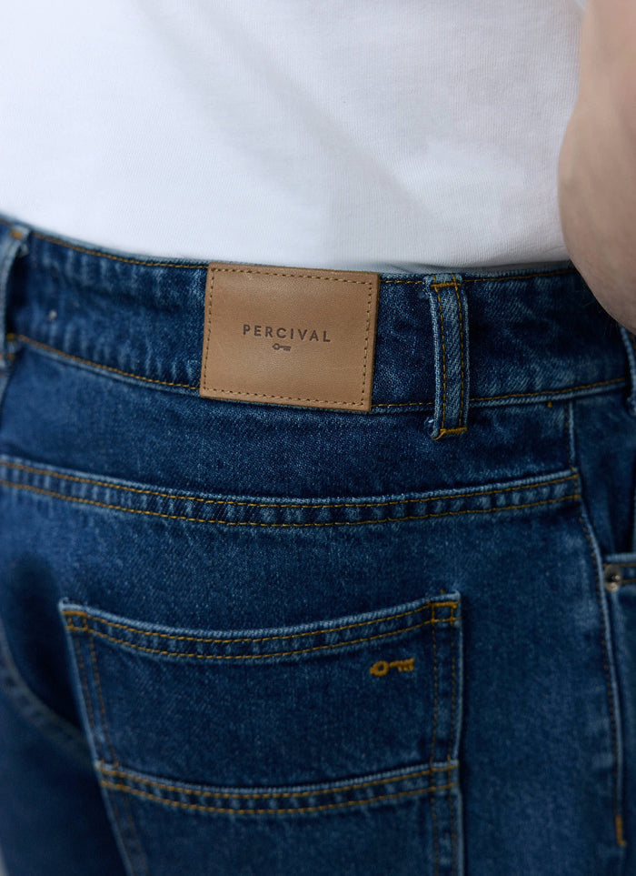 A close-up of the brown leather logo patch on the back of the Percival Wide Leg Denim Jeans in mid wash blue.