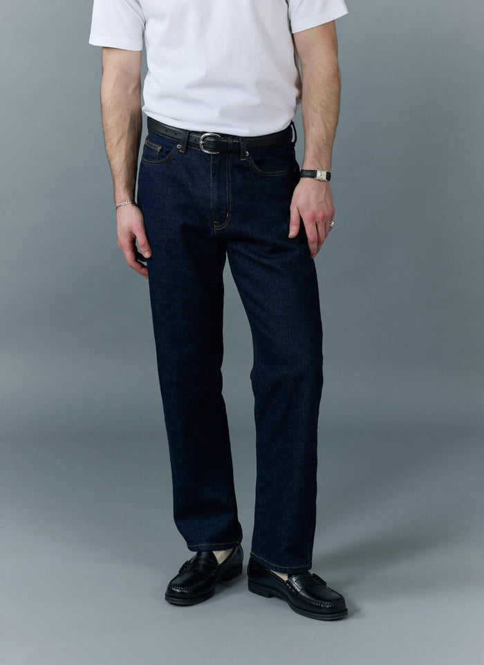 A model wears the Percival Straight Leg Denim Jeans in dark indigo, styled with a white t-shirt and black loafers.