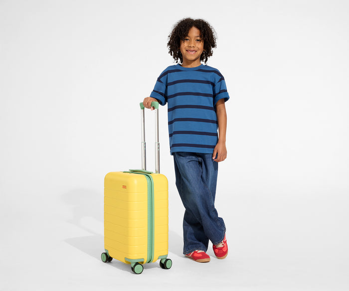 A child model is standing next to The Kids Carry-On suitcase in Sunshine Yellow and holding onto the raised handle to show size and scale
//
Daniel, age 8, with The Kids Carry-On in Sunshine Yellow.