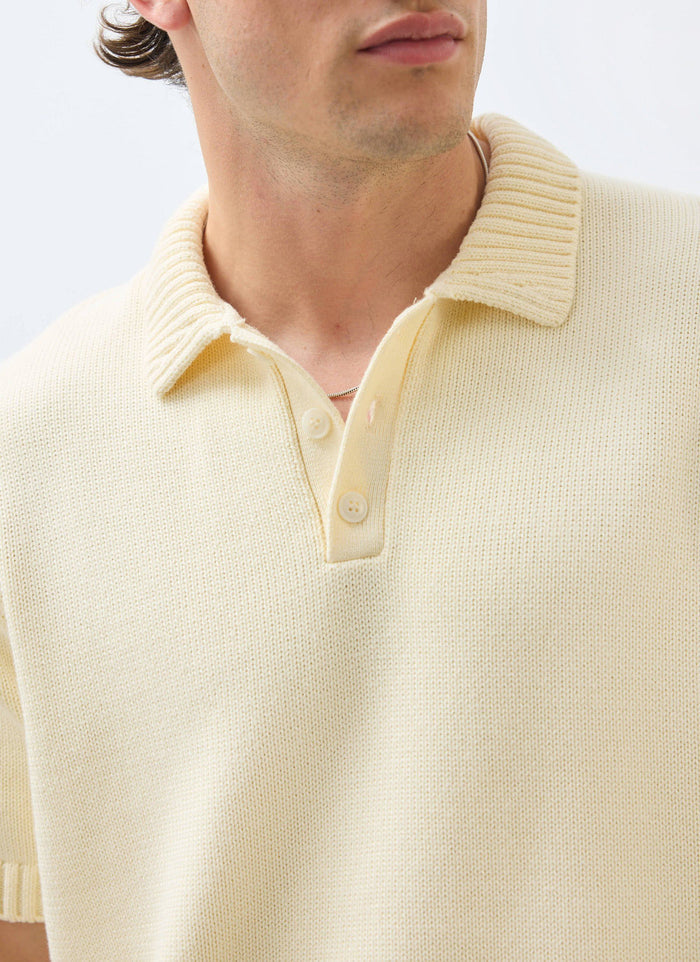 Close-up of a man wearing the ecru cotton Verso knitted polo shirt from Percival, showing the ribbed collar and buttons.